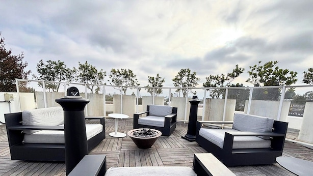 A rooftop terrace with modern outdoor furniture, including sofas and a round table, surrounded by a wooden deck and a view of the city skyline. - Cozy Modern Studio on Spaulding Ave – Complimentary WiFi & Parking (Los Angeles)