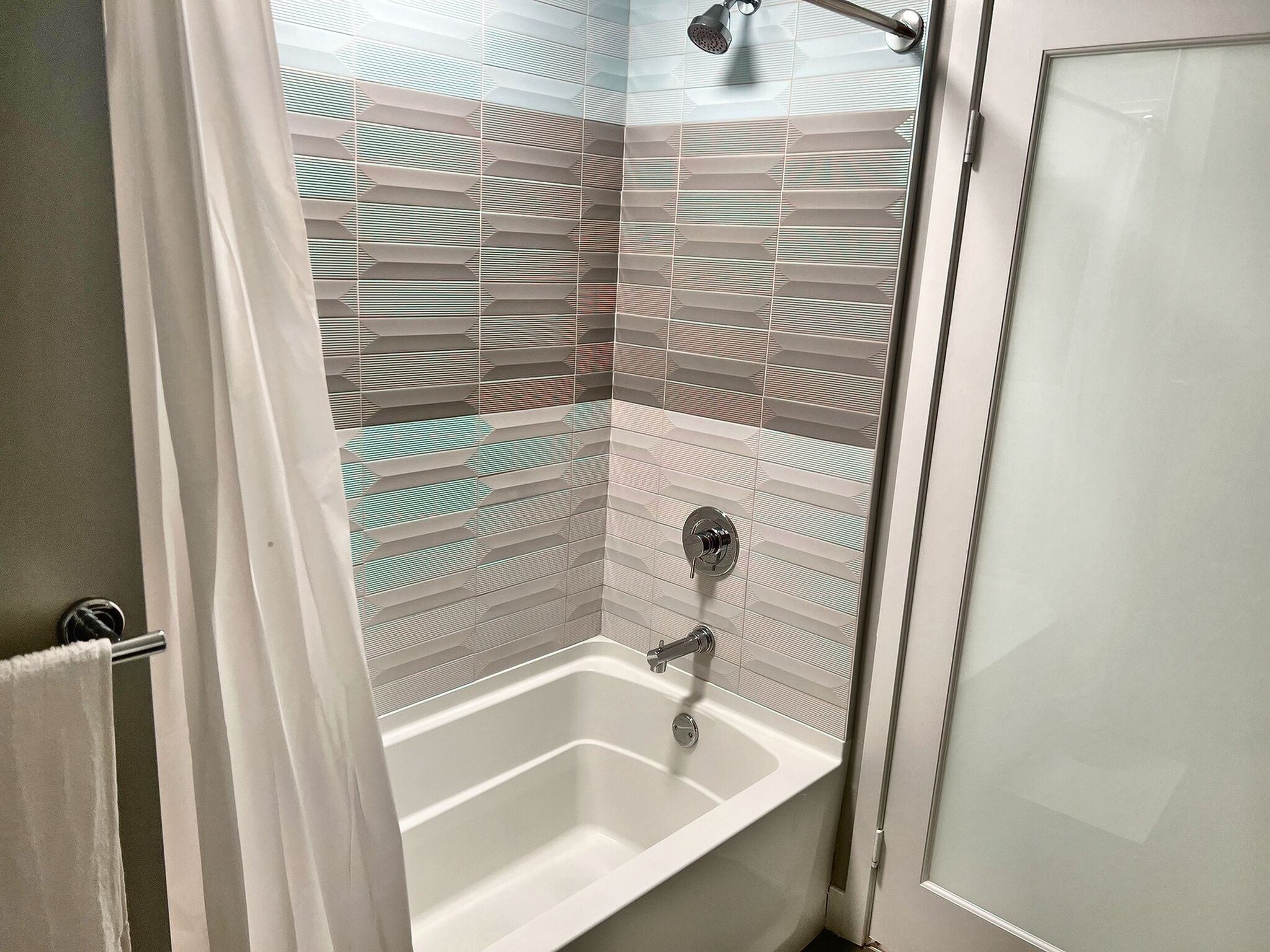 A bathroom with a shower, a bathtub, and a tiled wall with a geometric pattern.