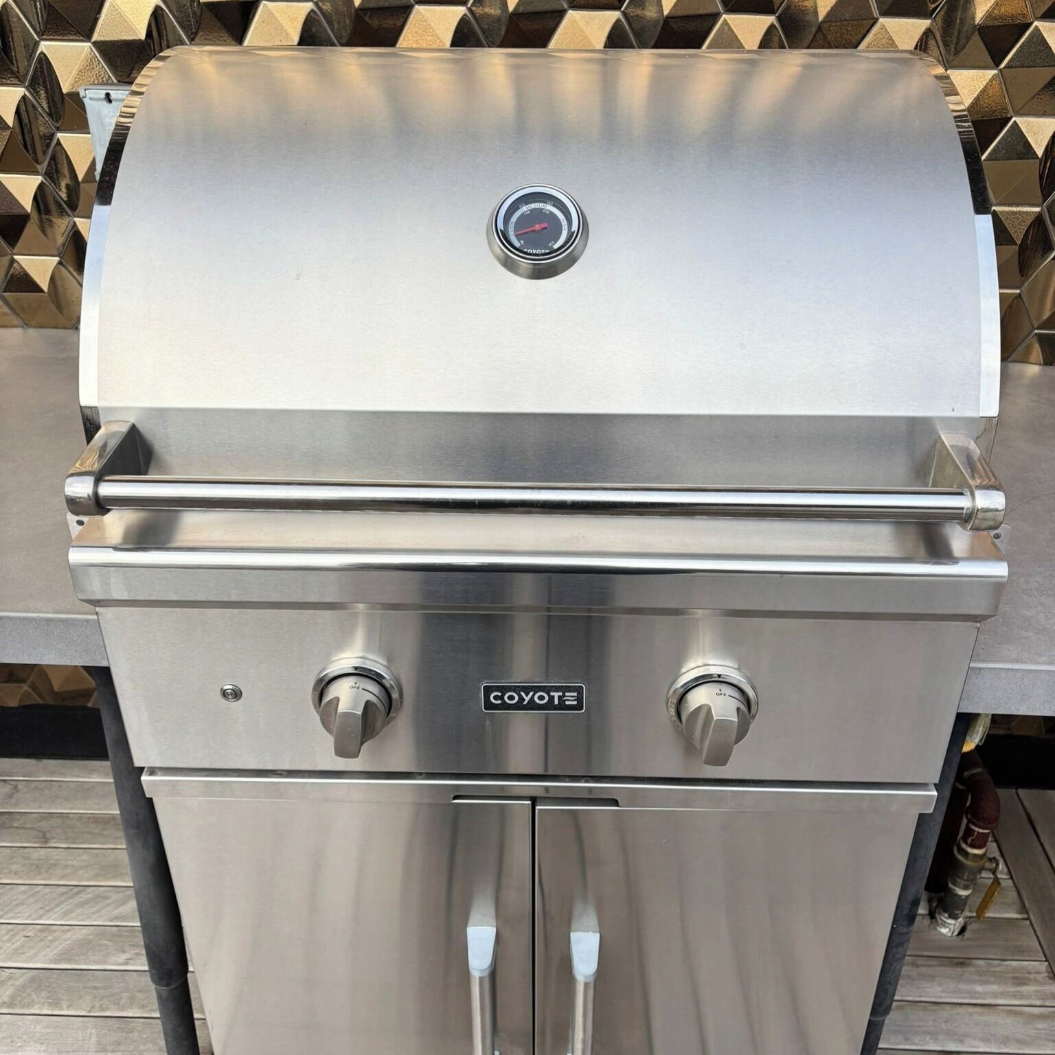 Un barbecue Coyote en acier inoxydable, doté d’un thermomètre numérique et de deux boutons de réglage.