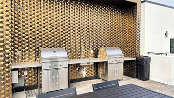 Ein Grillbereich im Freien mit zwei Grills, einem Spülbecken und einem Mülleimer.