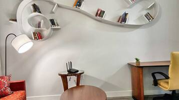 A modern room with a curved bookshelf, a round wooden table, a red sofa, a desk with a chair, and a floor lamp.