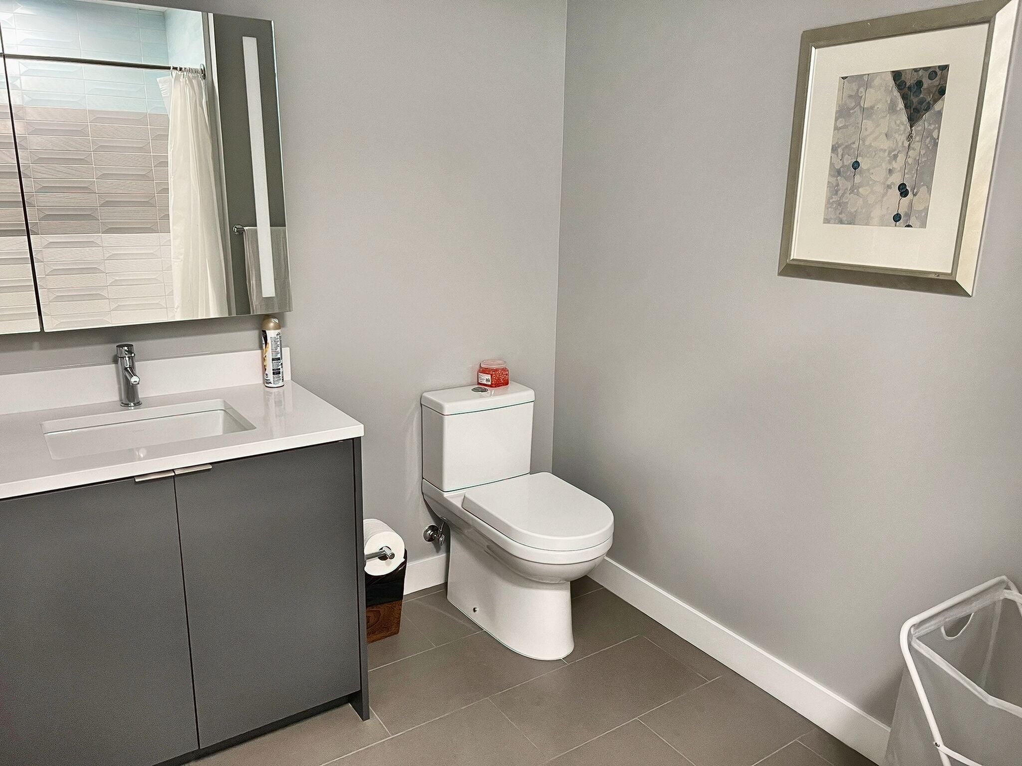 A modern bathroom with a white sink, a toilet, and a framed abstract painting on the wall.