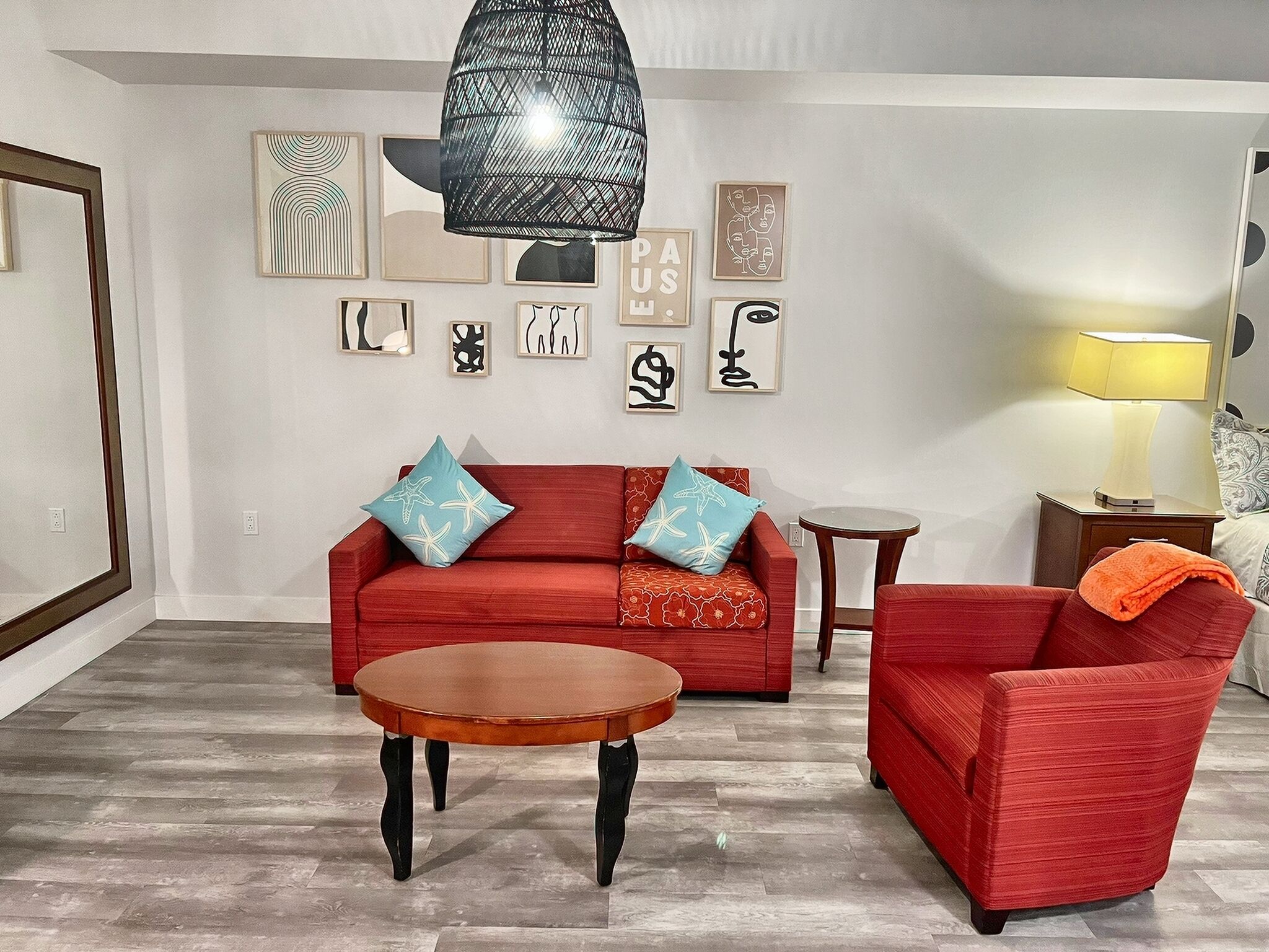 Una sala de estar con un sofá rojo, dos sillones a juego, una mesa de centro de madera y una mesita auxiliar. El piso es de baldosas y las paredes están decoradas con cuadros enmarcados.