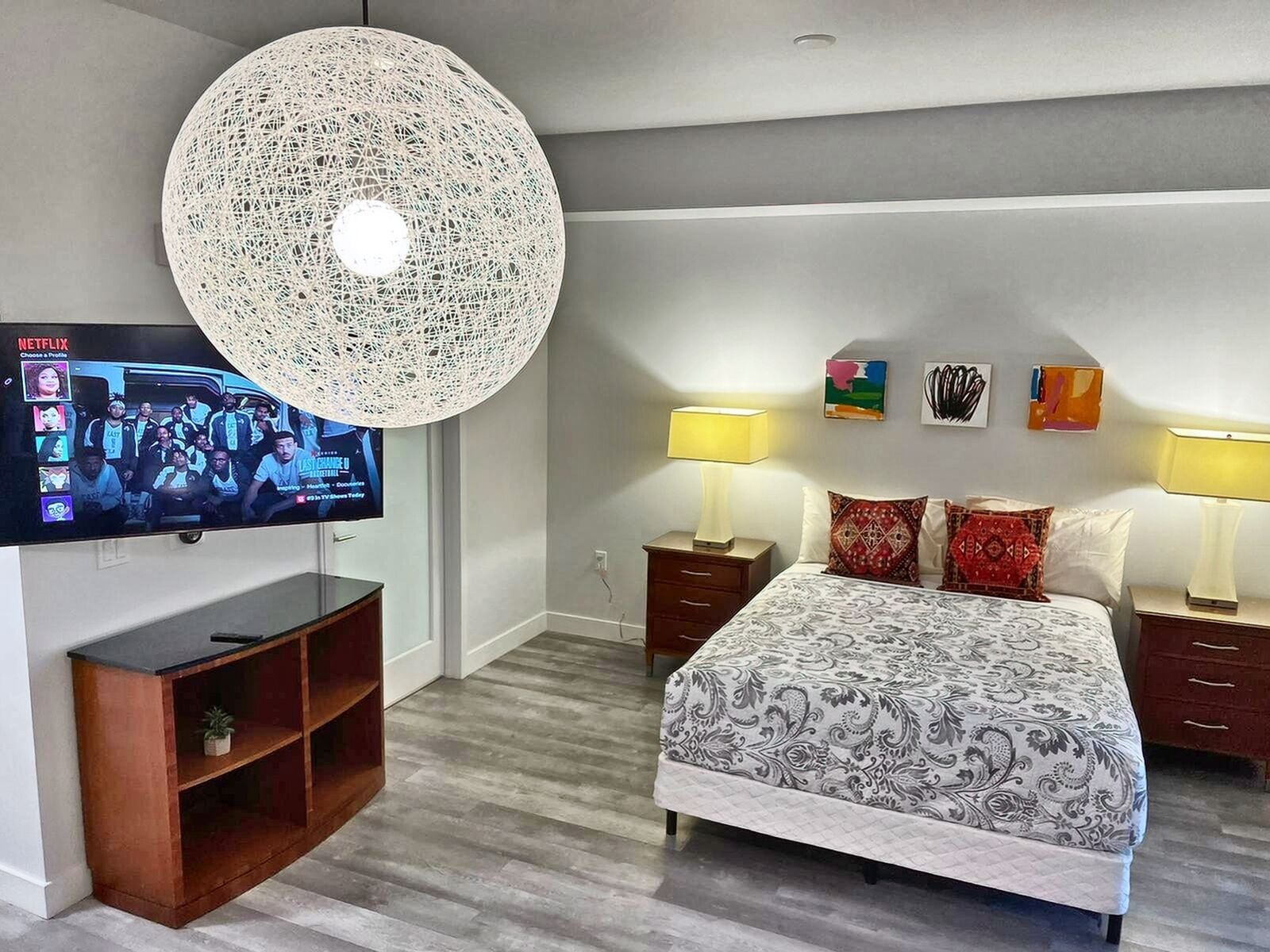 A modern hotel room with a large bed, two bedside tables with lamps, a TV mounted on the wall, and a decorative ceiling light.