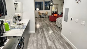A modern kitchen with a built-in oven and microwave, a dining area with a table and chairs, and a bedroom with a bed and a nightstand. - Cozy Modern Studio on Spaulding Ave – Complimentary WiFi & Parking (Los Angeles)