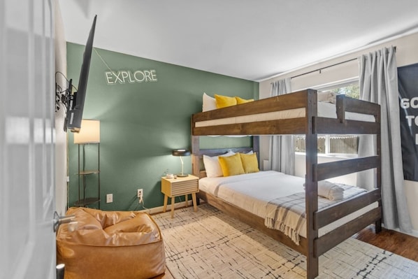 Habitación con literas, una pared verde, una lámpara, una mesita pequeña y un sillón de peluche.