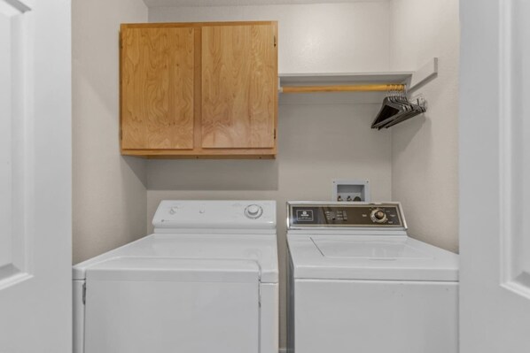 Une buanderie équipée de deux lave-linge à chargement frontal blancs et d’un meuble en bois placé au-dessus.