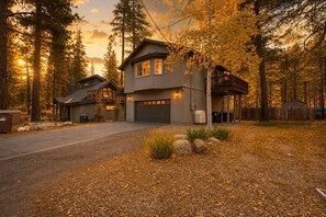 A two-story house with a garage, surrounded by a forest with autumn foliage.