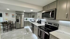 A modern kitchen with stainless steel appliances, a marble countertop, and a dining area with a table and chairs. - Boston 3BDR/2BA/10-min to Airport/ Free Parking (Revere)