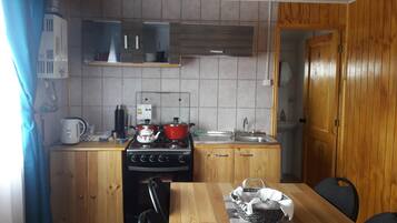 Una cocina compacta con armarios de madera, estufa, lavamanos y una mesa de comedor con sillas.