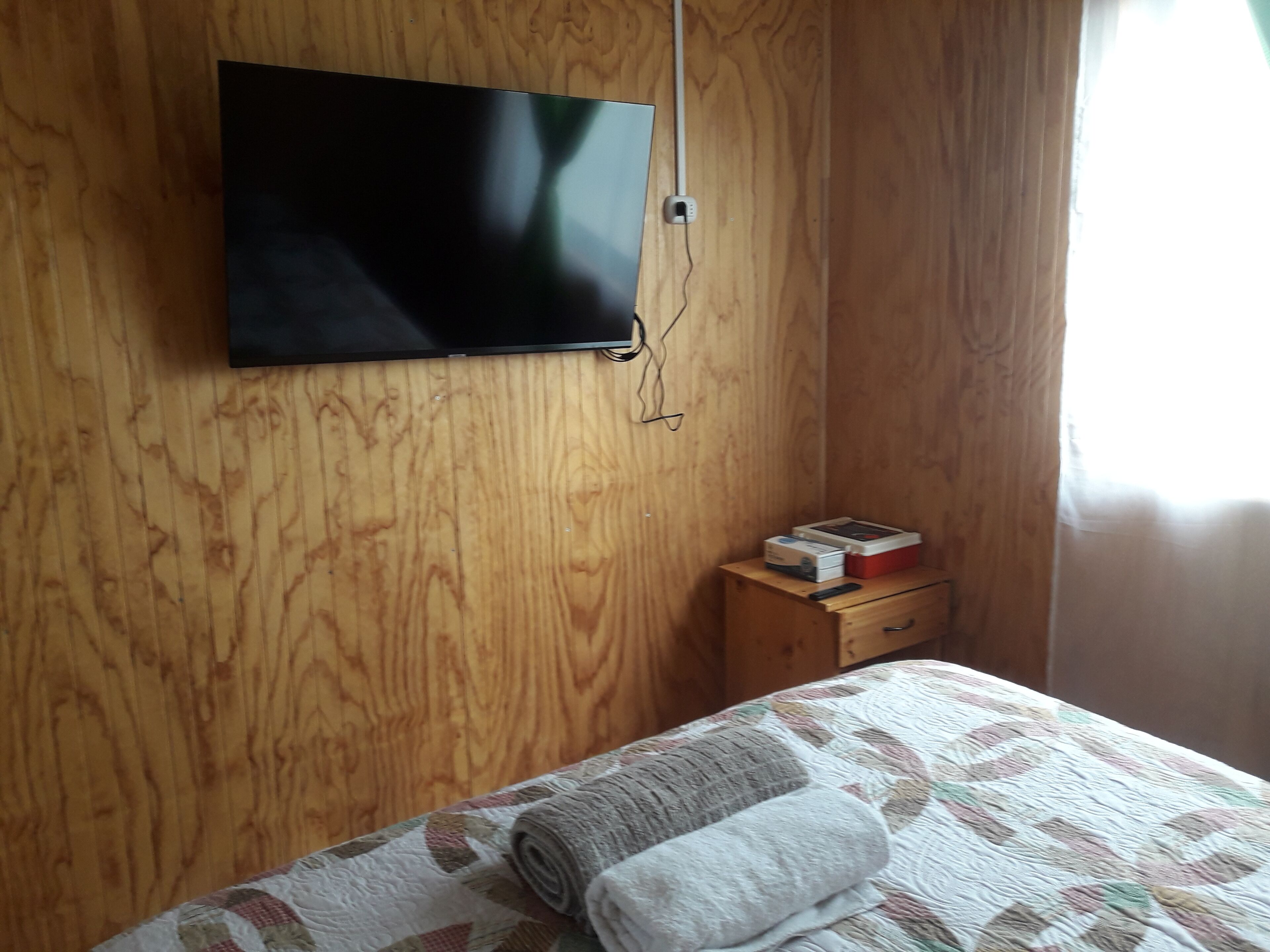 Een kamer met een houten wand, een flatscreen televisie boven een nachtkastje van hout, en een bed met een quilt.