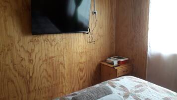 Een kamer met een houten wand, een flatscreen televisie boven een nachtkastje van hout, en een bed met een quilt.