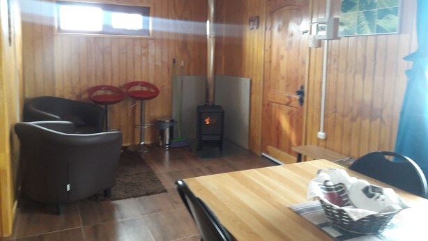 Een knus kamertje met houten wanden, een tafeltje met stoelen, een raam en een open haard.