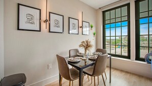 A dining area with a table set for four, framed artwork on the wall, and a large window with a city view. - Deep Ellum | 4 Ppl | Walkable | Great Views (Dallas)