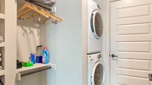 A laundry room with two stacked washing machines, a shelf with cleaning supplies, and a wooden drying rack with clothes. - Deep Ellum | 4 Ppl | Walkable | Great Views (Dallas)