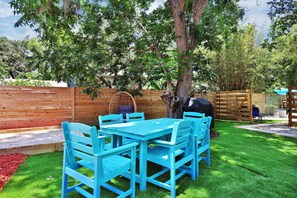 Un patio con una mesa y sillas azules, una cerca de madera y un árbol.