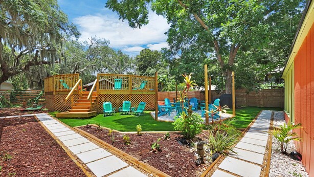 Un jardin avec une cabane en bois pour les enfants, une petite piscine et un espace patio aménagé avec des chaises.