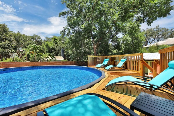 Ein Pool mit Holzterrasse, Liegestühlen und einem Holzzaun.
