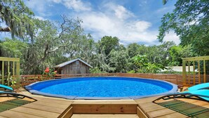 Une terrasse en bois avec une piscine, entourée d’arbres et d’une clôture en bois.