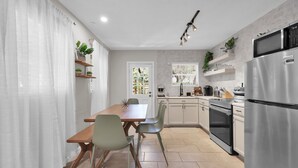 Une cuisine moderne avec des meubles blancs, un réfrigérateur en acier inoxydable et un coin repas comprenant une table et des chaises en bois.