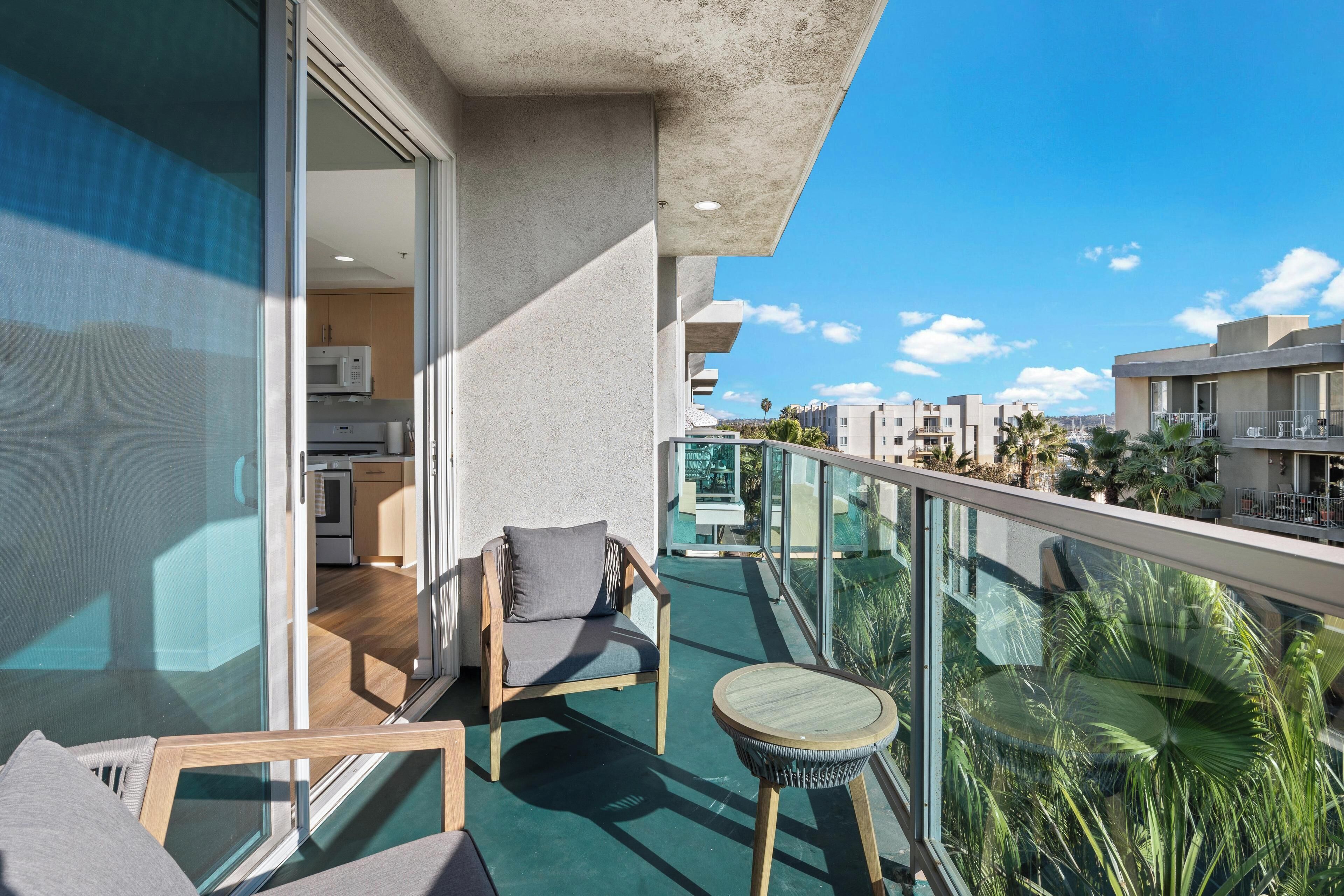 A balcony with a glass door leading to a kitchen, a wooden chair, and a small round table.