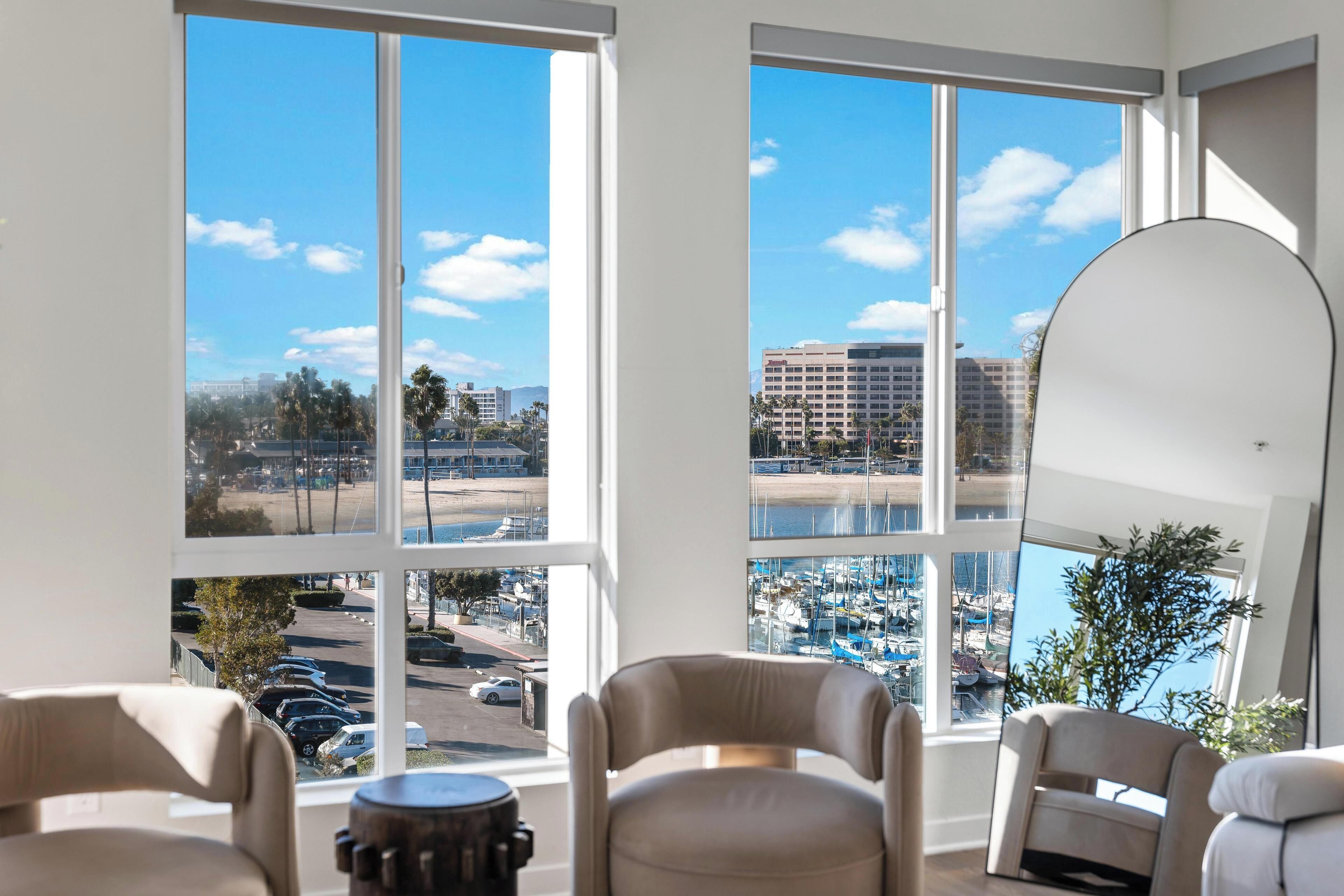 A room with large windows offering views of a marina and cityscape. There are two chairs and a round table.