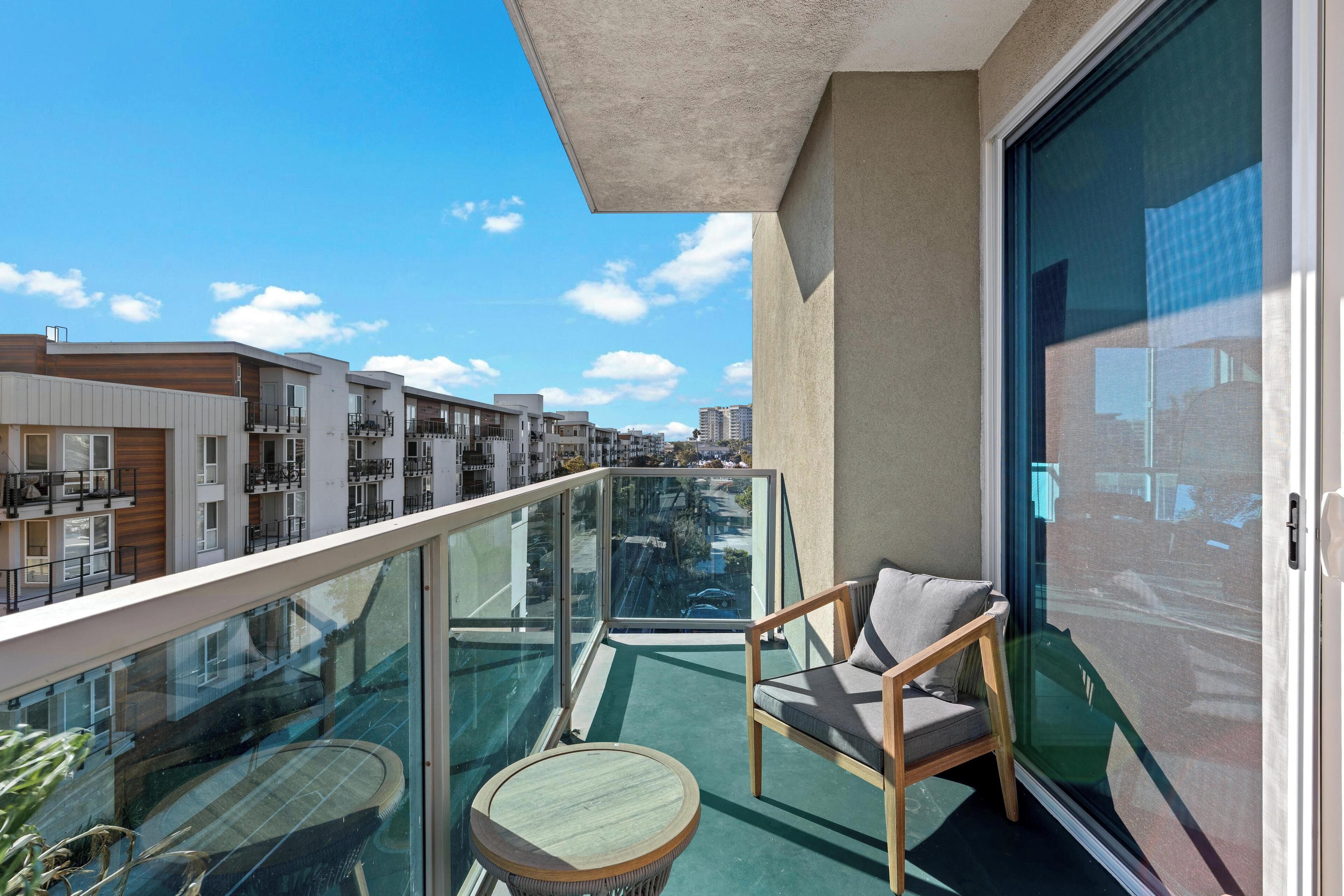Een balkon met glazen hekwerk, een stoel en een tafeltje.