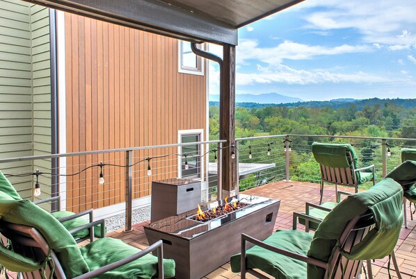 A balcony with a fire pit, green chairs, and a view of a wooden building and mountains.