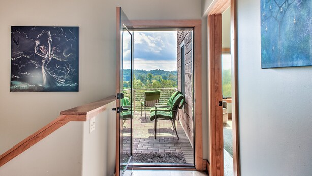 En trappe fører op til en balkon med grønne stole, et maleri på væggen og udsigt over landskabet.