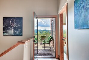 Un escalier menant à un balcon agrémenté de chaises vertes, un tableau accroché au mur et une vue sur le paysage.