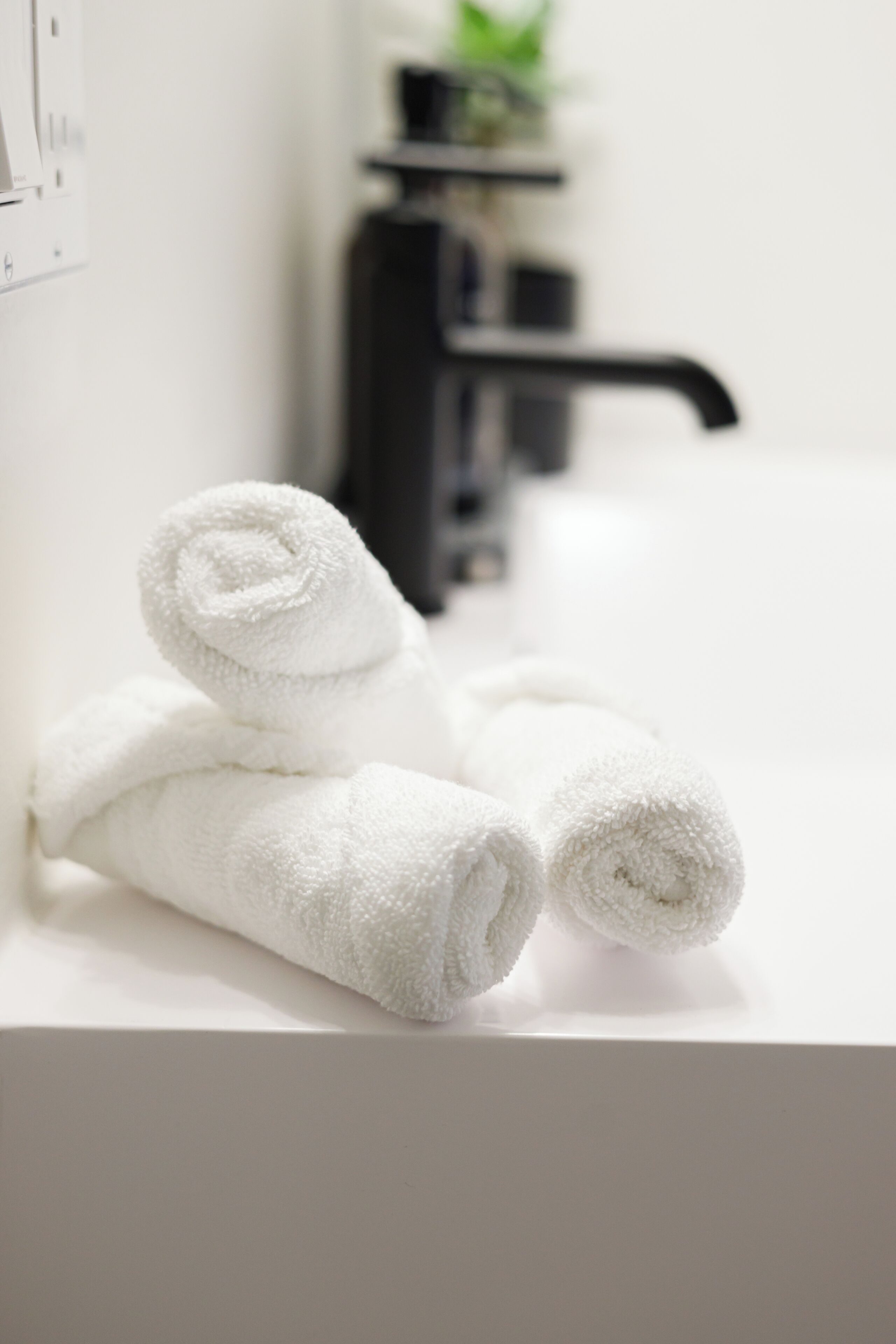 A white bathroom sink with two rolled white towels placed on it.