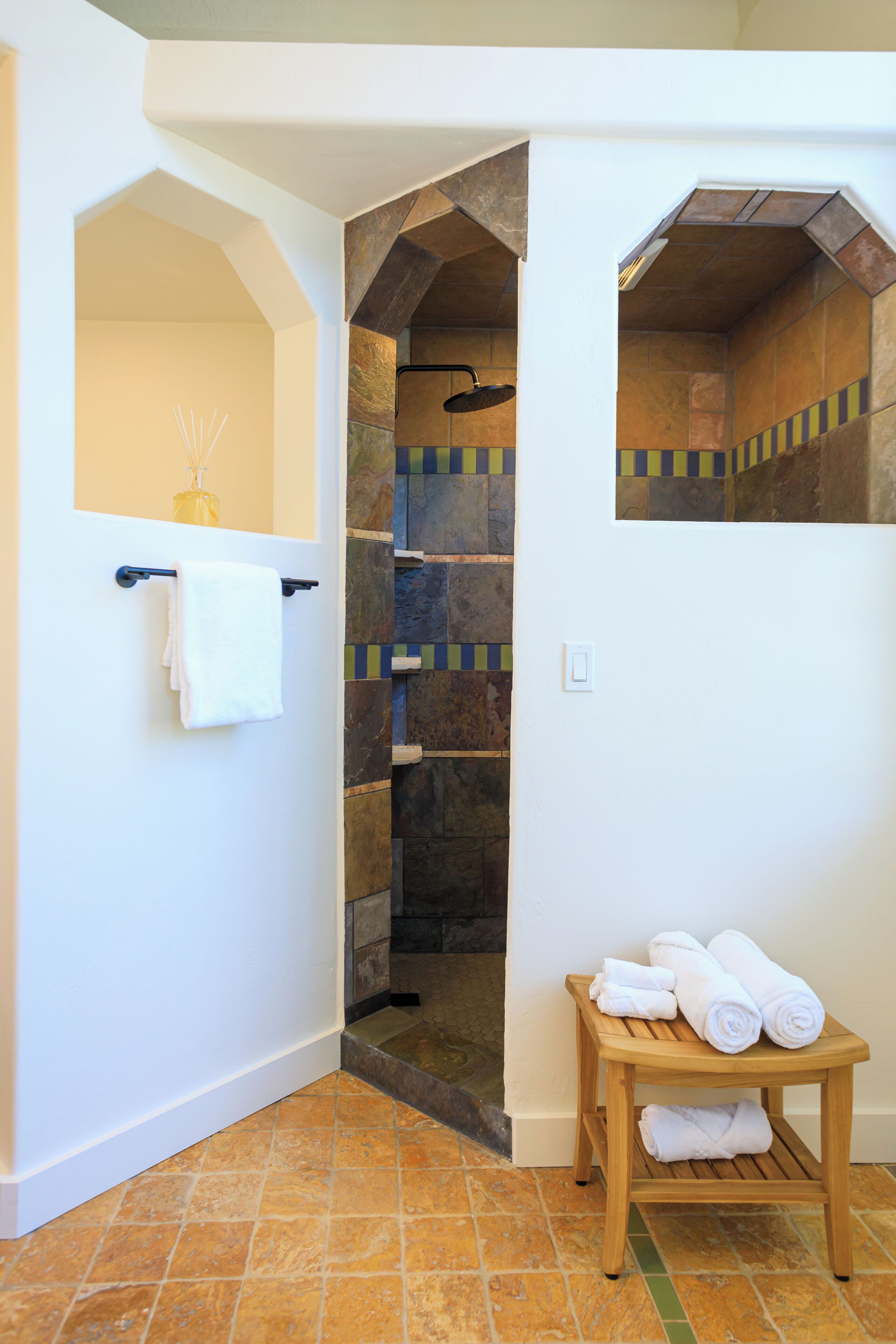 A bathroom with a white sink, a towel rack, and a wooden stool with rolled towels.