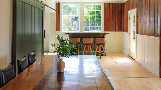 A dining area with a long wooden table, chairs, a vase with a plant, and a sliding barn door. - The Historic Schoolhouse Inn   (Trinidad)