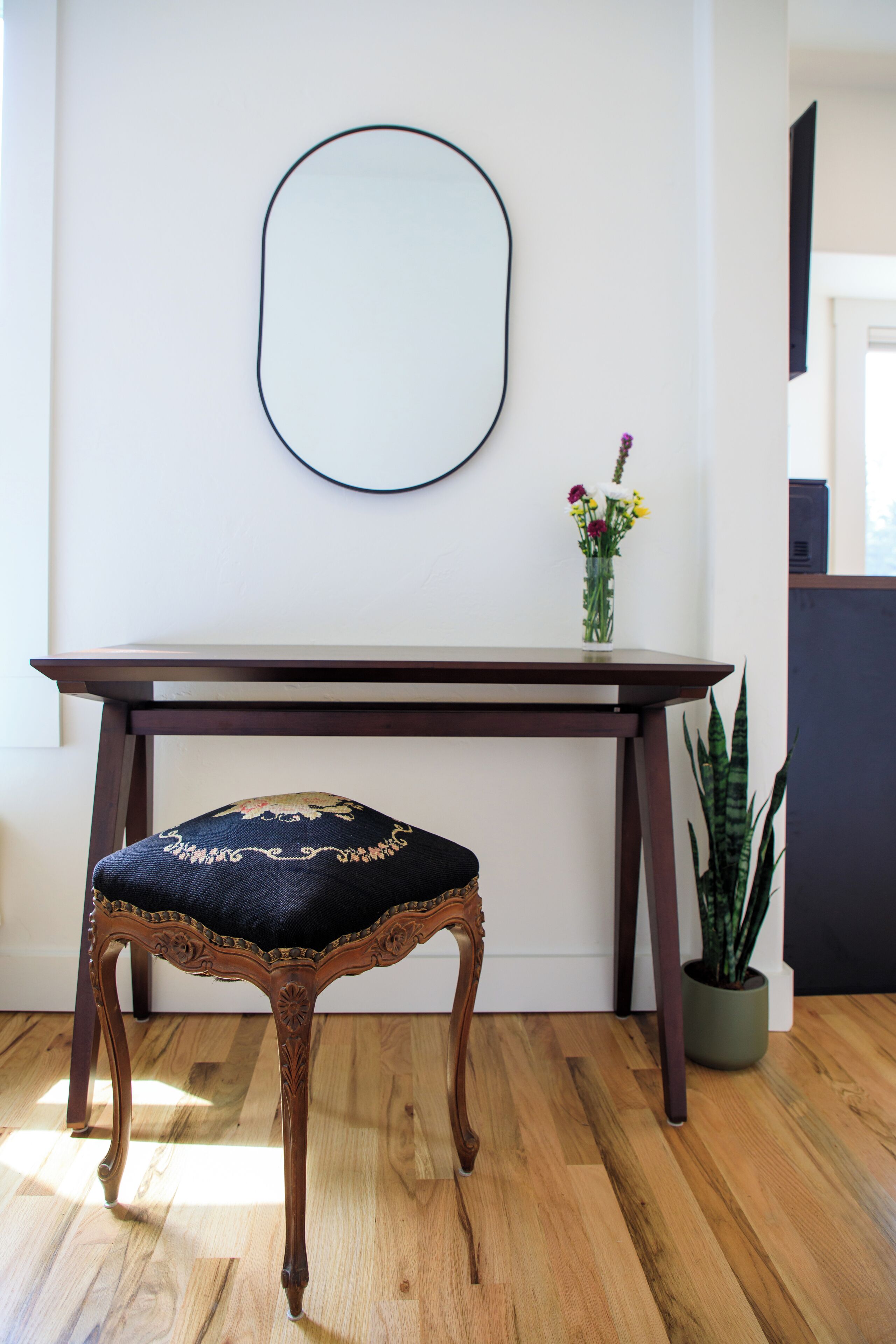 Una mesa de madera con una silla tapizada oscura, una planta en maceta y un espejo fijado a la pared.