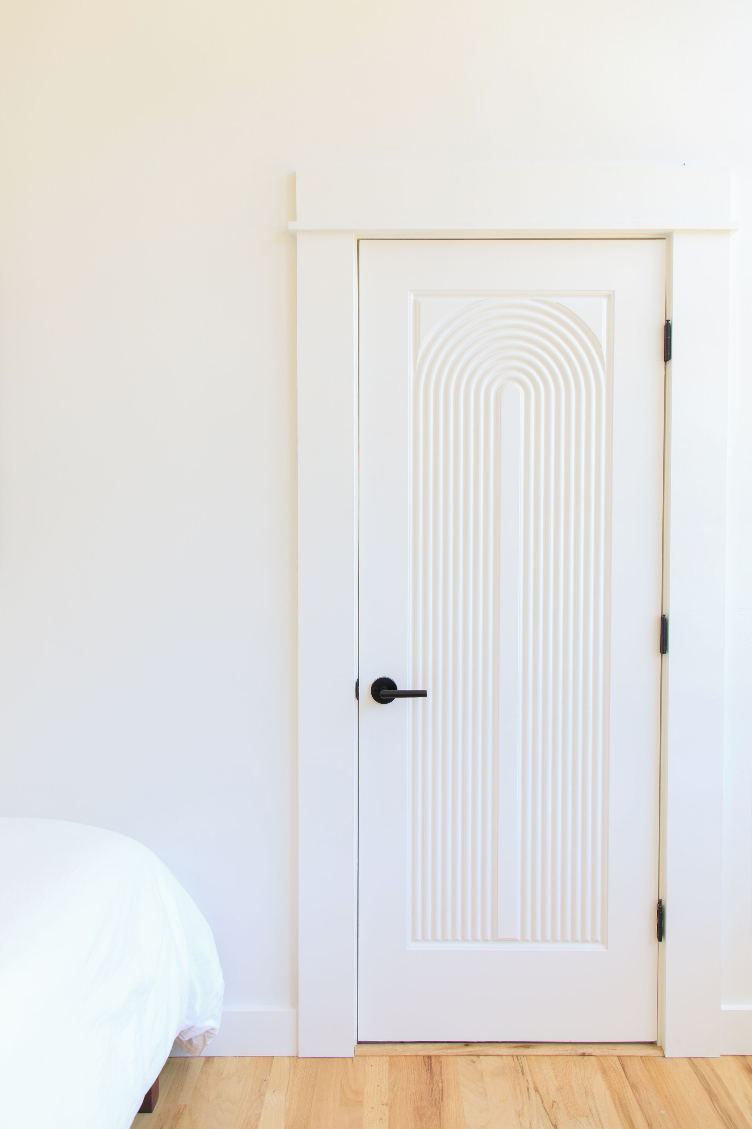 A white door with a geometric pattern, a bed with a white cover, and wooden flooring.