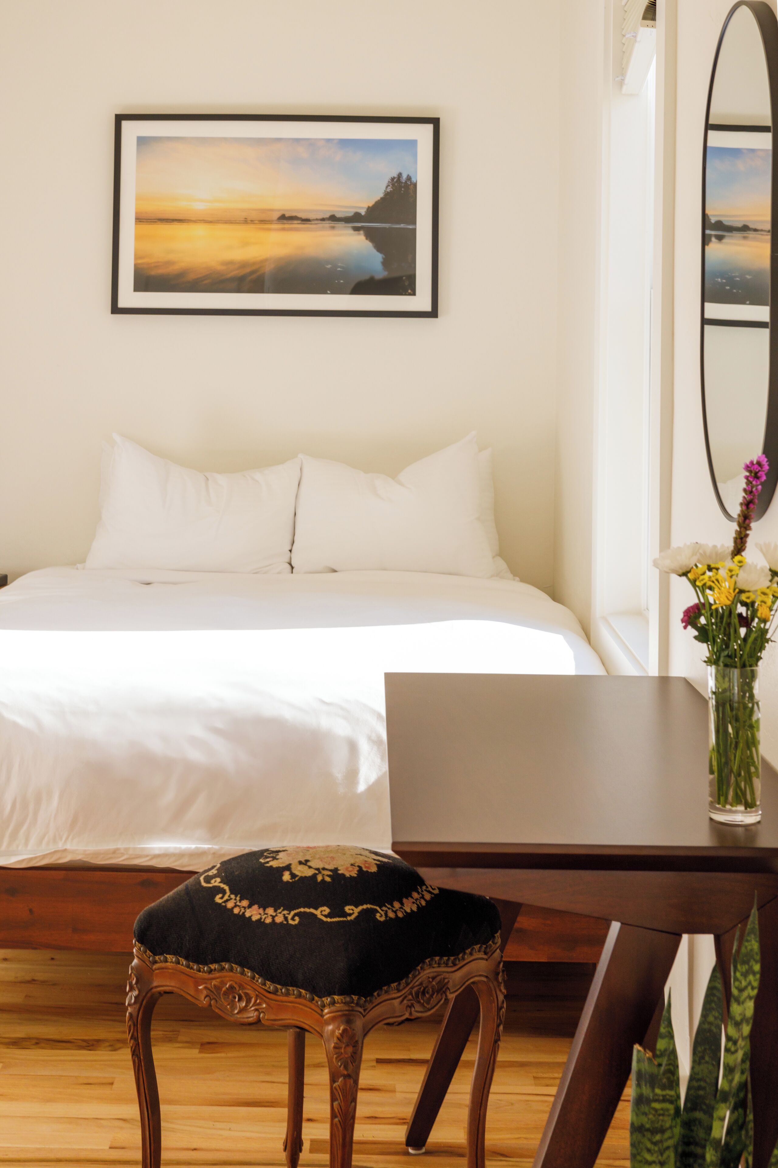 Une chambre à coucher bien rangée, avec un lit, une table de chevet ornée d’un vase de fleurs et un tableau encadré accroché au mur.