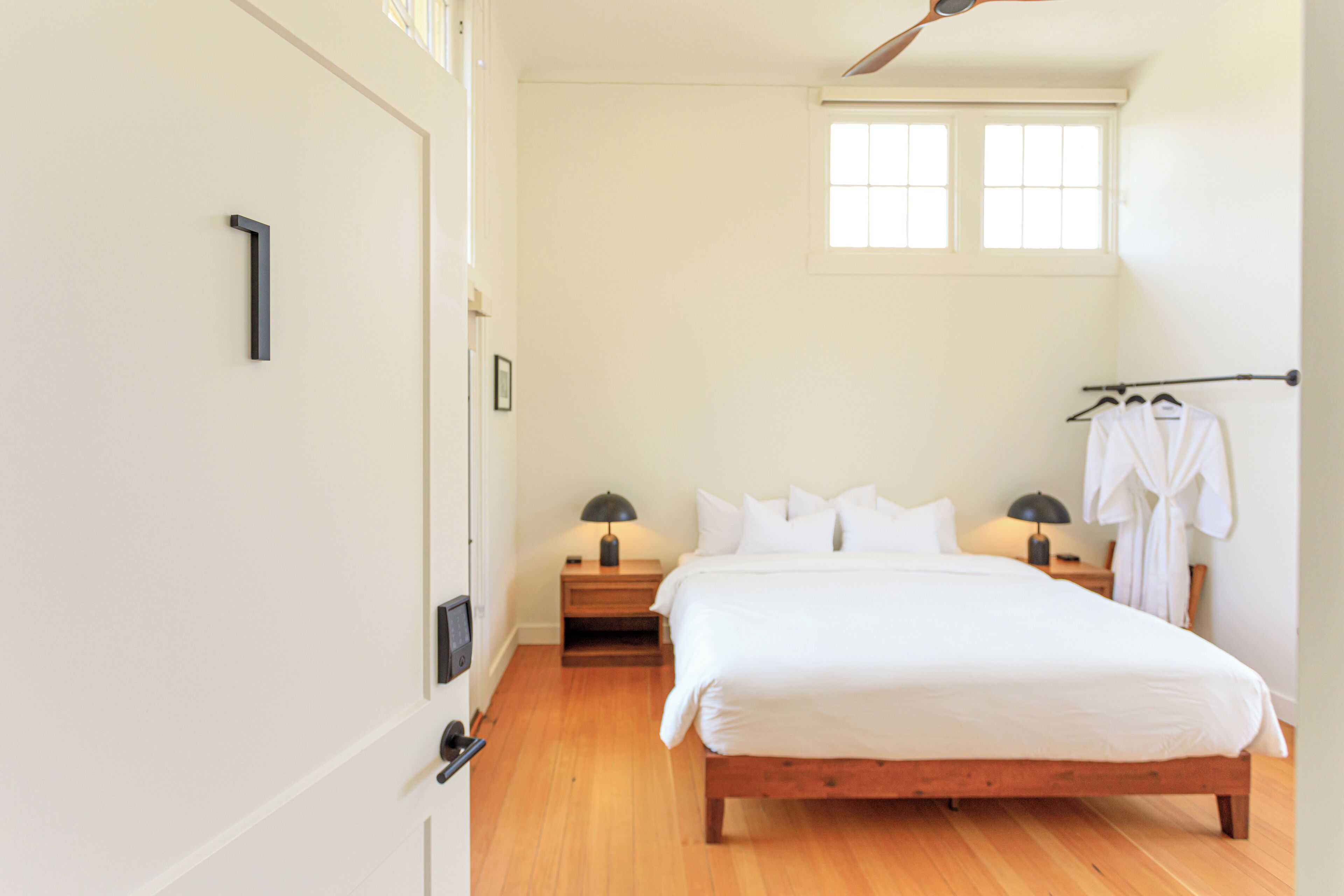 A bedroom with a wooden bed, bedside tables with lamps, a window, and a robe rack.