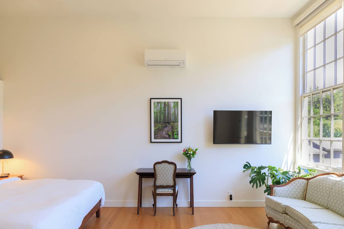 A bedroom with a bed, a desk, a chair, a TV, and a window with a view of trees.