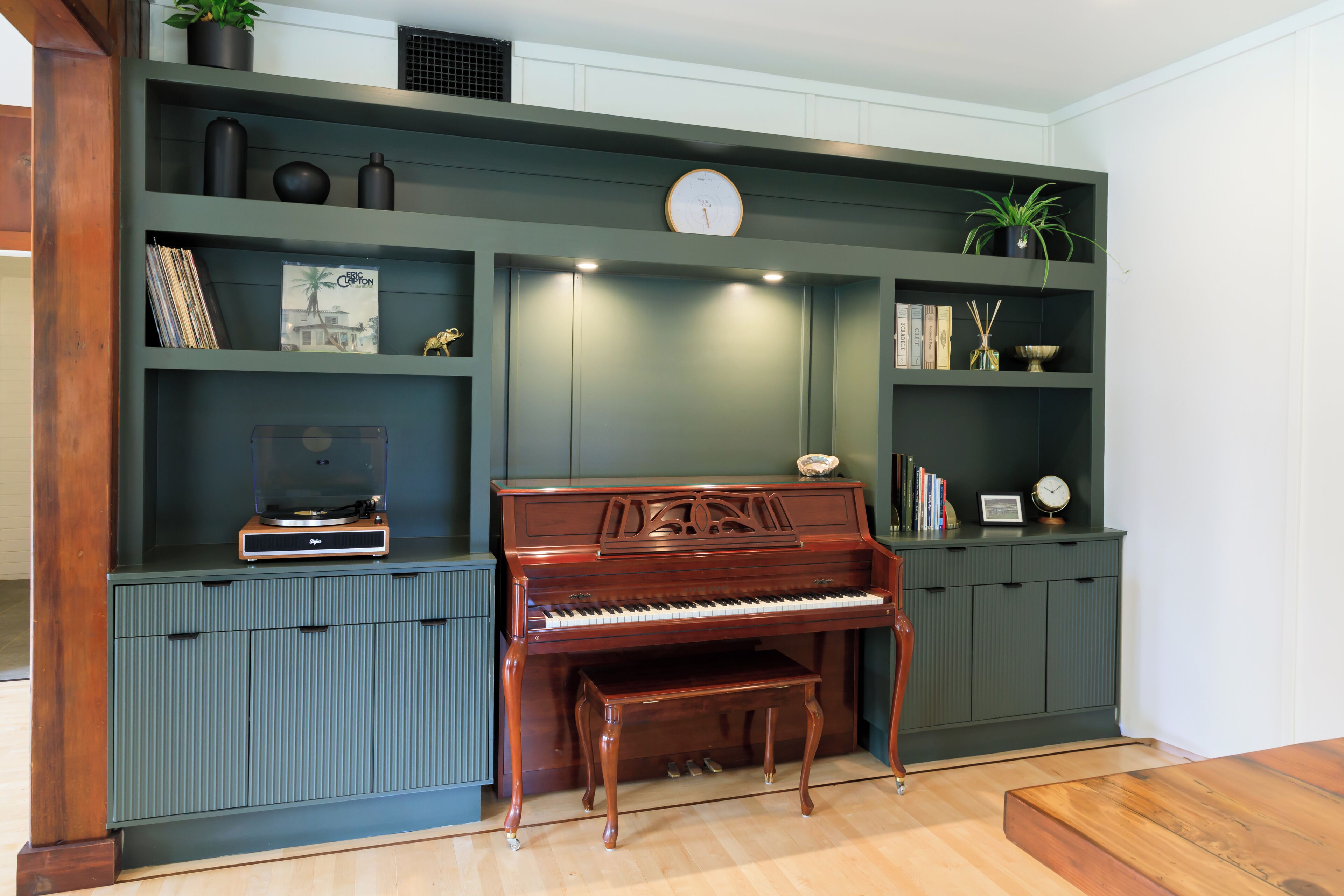 Um quarto com um piano de cauda, uma estante de livros e um relógio na parede.