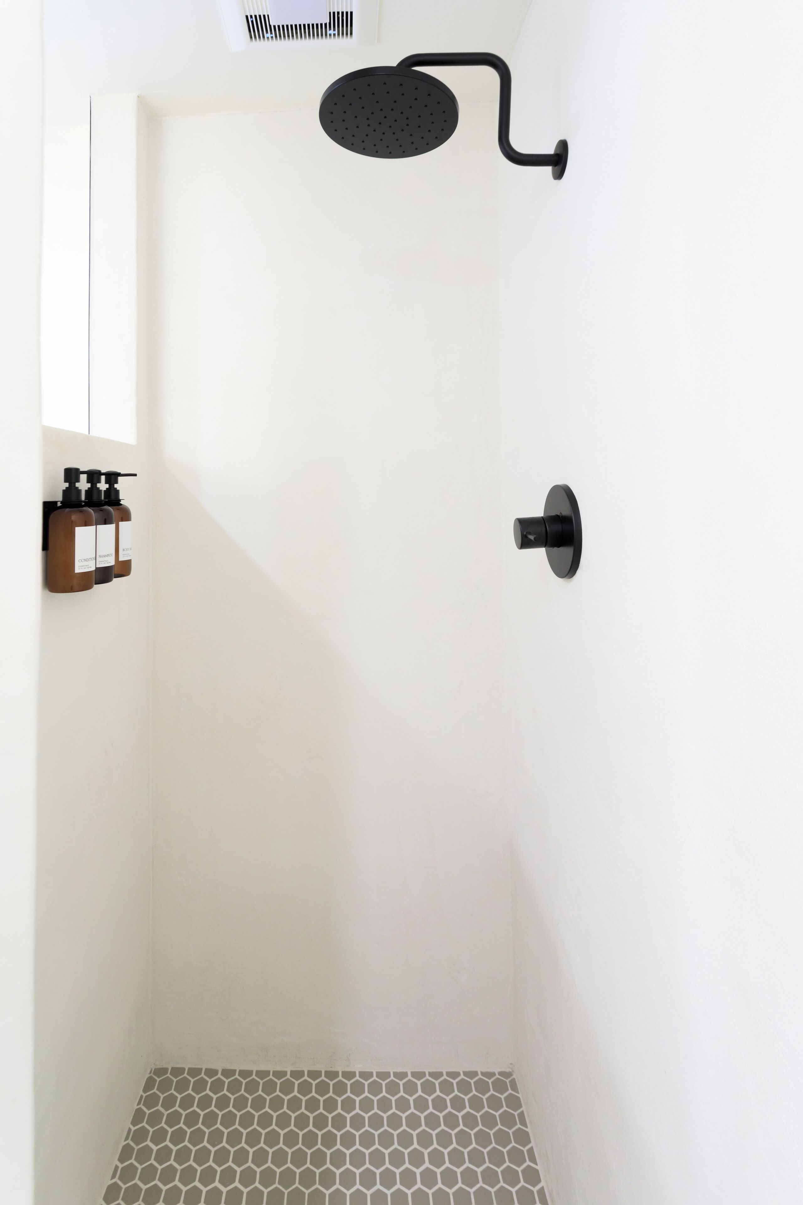 A minimalist shower area with a black showerhead and a hexagonal tile floor.