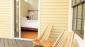 A wooden deck with two lounge chairs, a bed with white linens, and a hanging light fixture. - The Historic Schoolhouse Inn   (Trinidad)