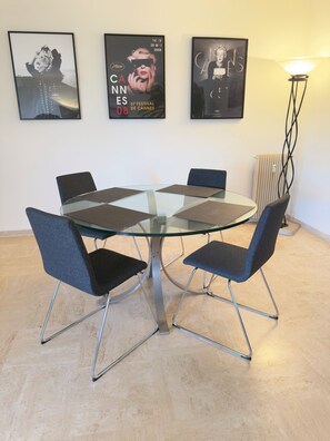 A round glass table with four chairs, a poster of the Cannes Film Festival, and a floor lamp. - Marilyn Beach - Sea view, terrace & private garage (Cannes)
