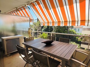 An outdoor patio with a table and chairs, a ceiling fan, and a view of greenery and buildings. - Marilyn Beach - Sea view, terrace & private garage (Cannes)