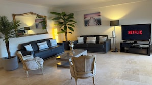 En moderne stue med sofa, lænestole, sofabord, fjernsyn og en stor plante.
