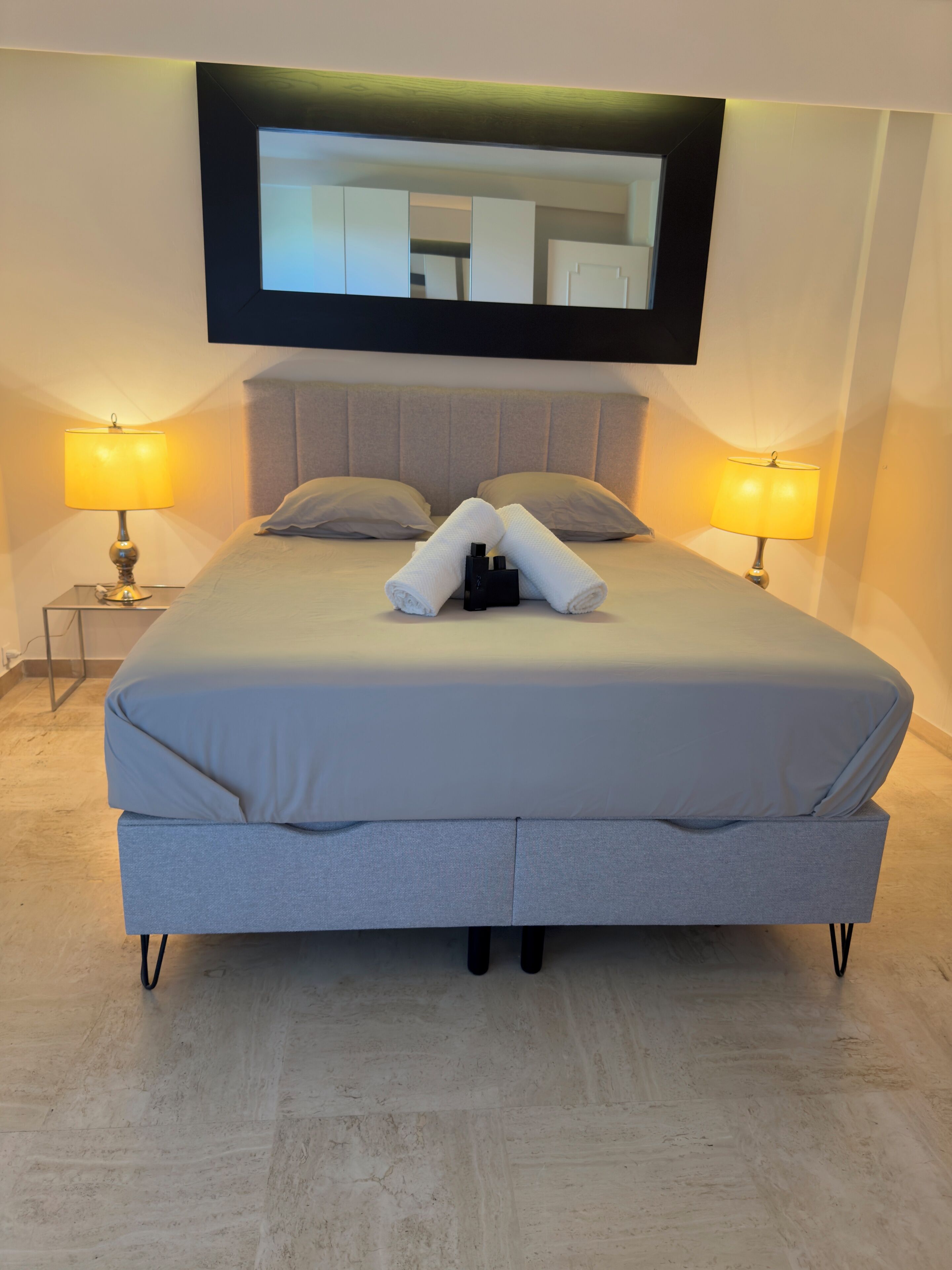 Una camera d'albergo moderna con un letto grande, due lampade ai comodini, una TV a schermo piatto montata a parete e un tavolino con lampada.