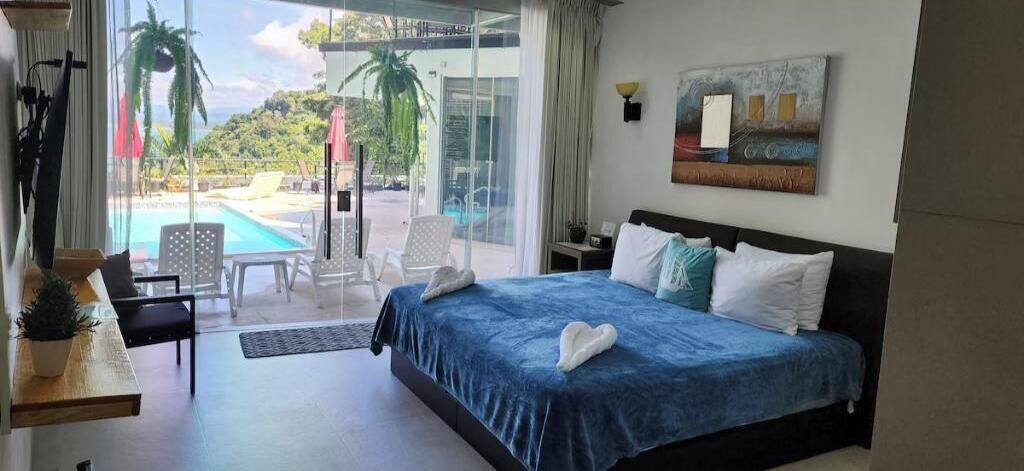 Habitación de hotel con cama, escritorio, silla y vistas a una piscina y vegetación.