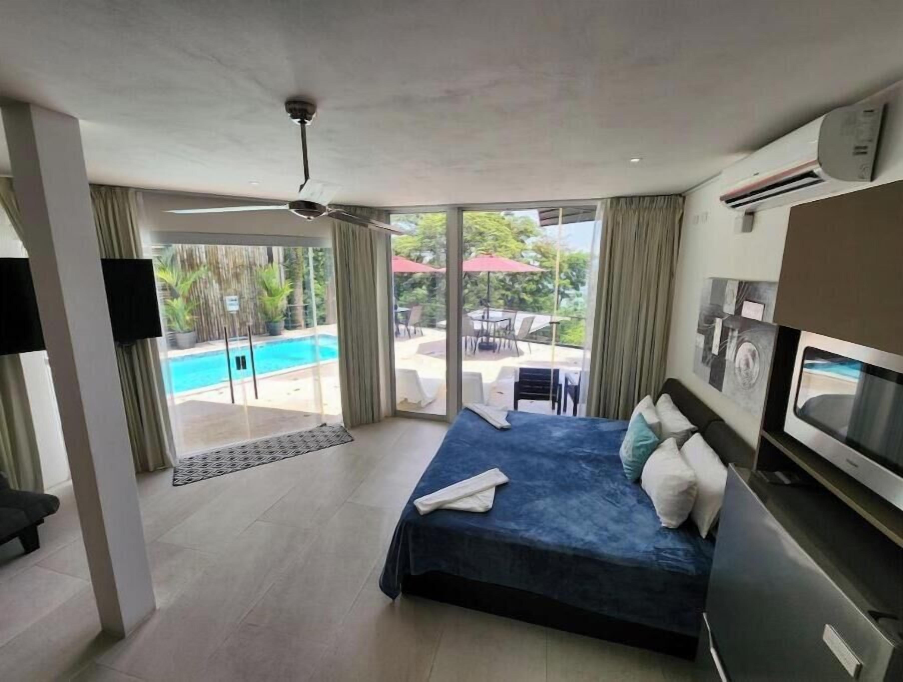 Une chambre d’hôtel moderne dotée d’un grand lit, d’une télévision et d’une porte-fenêtre coulissante donnant sur un espace piscine.