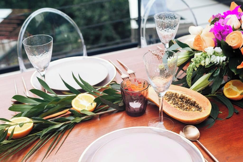A table set for a meal with clear glassware, plates, and a decorative centerpiece including flowers and a papaya.