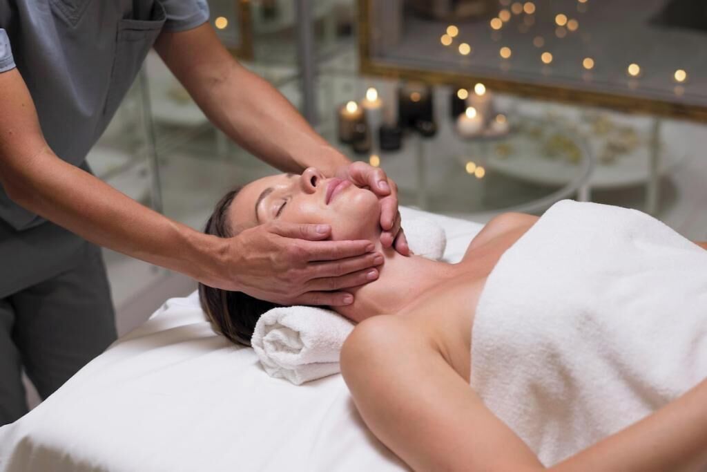 En person får en ansiktsmassage i en spa-miljö, med tända ljus i bakgrunden.