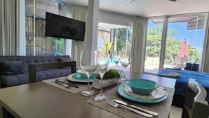 Habitación de hotel moderna con comedor, sofá, televisor montado en la pared y balcón con vistas al exterior.